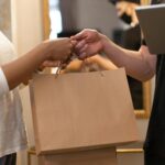 Two people exchanging a shopping bag in an indoor setting highlighting online shopping and delivery.